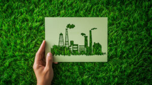A hand holds a drawing of an industrial building using green energy over a field of grass.
